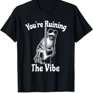 Puede incluir: Camiseta negra con un dise&ntilde;o blanco de una rana con gafas de sol sosteniendo un poste. El texto "You're Ruining The Vibe" est&aacute; arriba y abajo de la ilustraci&oacute;n.