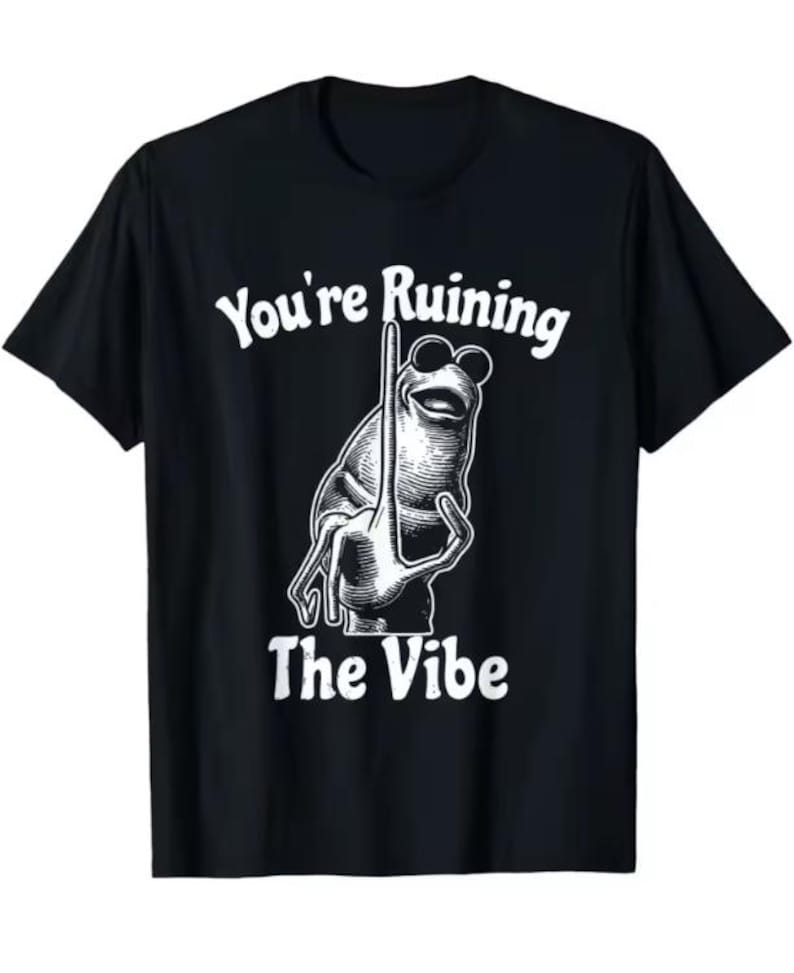 Puede incluir: Camiseta negra con un dise&ntilde;o blanco de una rana con gafas de sol sosteniendo un poste. El texto "You're Ruining The Vibe" est&aacute; arriba y abajo de la ilustraci&oacute;n.