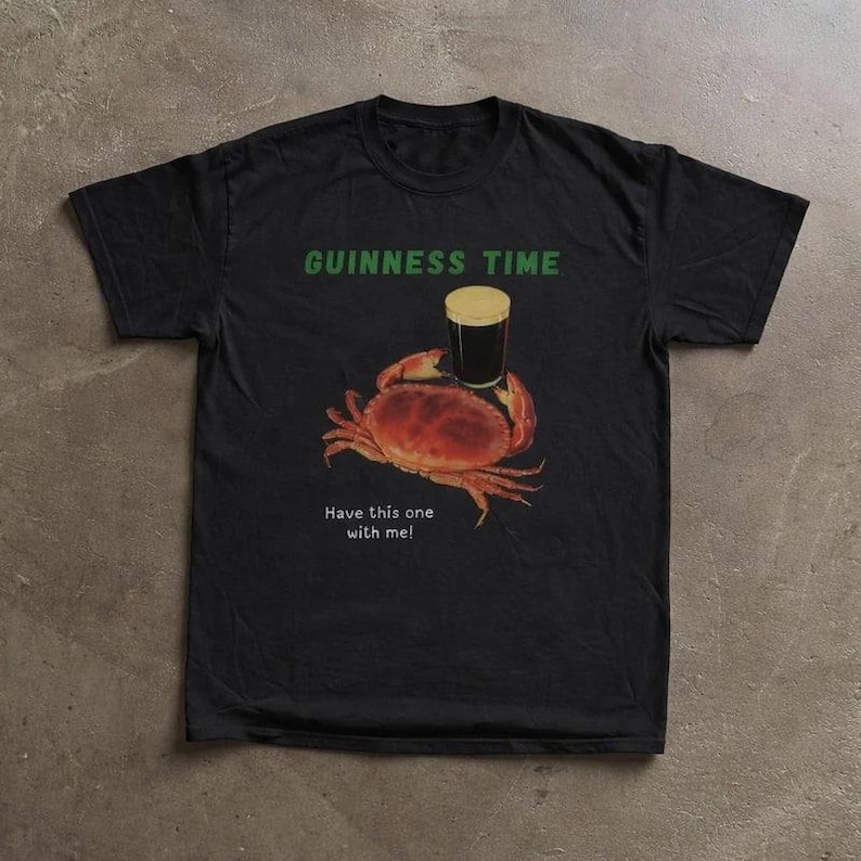 May include: Black t-shirt with a graphic of a crab holding a pint of Guinness. The text "GUINNESS TIME" is above the crab, and "Have this one with me!" is below. The crab is brown and the beer has a tan head.