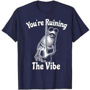 Puede incluir: Camiseta azul marino con un dibujo blanco de una rana con gafas de sol y un gesto con la mano. El texto "You're Ruining The Vibe" est&aacute; impreso encima y debajo de la ilustraci&oacute;n de la rana.