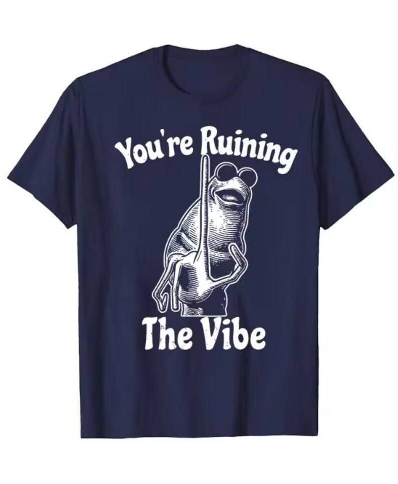 Puede incluir: Camiseta azul marino con un dibujo blanco de una rana con gafas de sol y un gesto con la mano. El texto "You're Ruining The Vibe" est&aacute; impreso encima y debajo de la ilustraci&oacute;n de la rana.