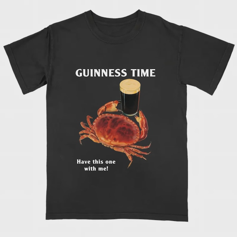 May include: Black t-shirt with a crab graphic holding a pint of stout. The text "GUINNESS TIME" is above the crab, and "Have this one with me!" is below. The crab is red-brown, and the beer has a tan head.