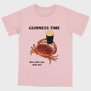 May include: Pale pink t-shirt featuring the text "GUINNESS TIME" above a crab holding a pint of Guinness. The text "Have this one with me!" is below the crab.