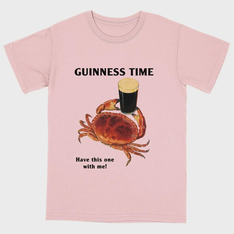 May include: Pale pink t-shirt featuring the text "GUINNESS TIME" above a crab holding a pint of Guinness. The text "Have this one with me!" is below the crab.