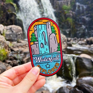 May include: A colourful embroidered patch with a cartoon illustration of a waterfall and the text "Waterfall Explorer" with a star.