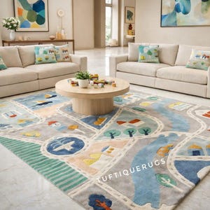 May include: A large area rug with a road map design in shades of gray, blue, and green. The rug features illustrations of houses, trees, and vehicles. Two beige sofas and decorative pillows are in the background.