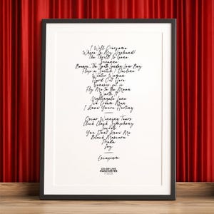K&ouml;nnte beinhalten: Schwarz-wei&szlig; gerahmter Druck mit handgeschriebenen Songtexten. Der Druck enth&auml;lt Songtitel wie "The Thrill Is Gone" und "Secrets". Der untere Teil des Drucks lautet "CO-OP LIVE MANCHESTER 17.02.26."