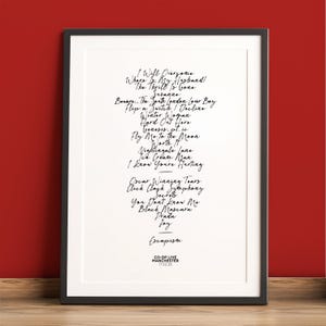 K&ouml;nnte beinhalten: Ein gerahmter Druck mit schwarzem Rahmen vor rotem Hintergrund. Der Druck zeigt handgeschriebene Songtitel in schwarzer Tinte, darunter "Escapism" und "Fly Me to the Moon". Der untere Teil des Drucks lautet "CO-OP LIVE MANCHESTER 17.02.26."
