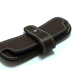 May include: A brown leather case with white stitching and a snap closure. The case is folded in half and has a strap.