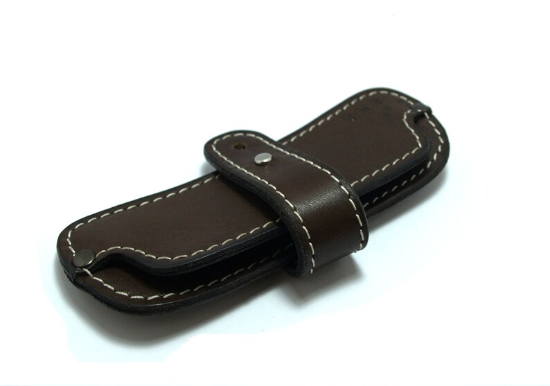 May include: A brown leather case with white stitching and a snap closure. The case is folded in half and has a strap.