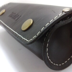 May include: A black leather roll-up case with white stitching and brass accents. The case has the word "itari" embossed on the front.