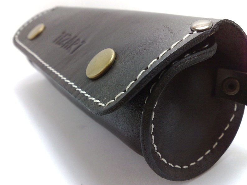 May include: A black leather roll-up case with white stitching and brass accents. The case has the word "itari" embossed on the front.