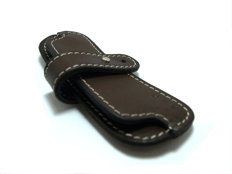 May include: A brown leather case with white stitching and a silver button. The case is designed to hold a small knife or other tool.