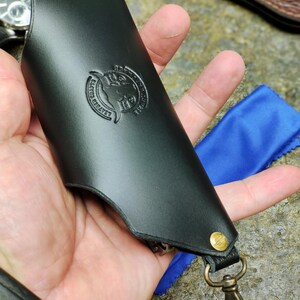 Puede incluir: Llavero de cuero negro con cierre y remaches de lat&oacute;n. El llavero presenta un emblema en relieve con el texto "LEATHER CRAFTS" y un dise&ntilde;o de cabeza de toro. Se ve un pa&ntilde;o de microfibra azul.