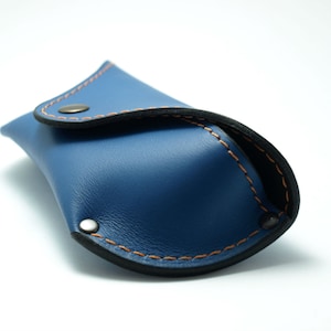 Puede incluir: Un estuche para gafas de cuero azul con costuras naranjas y ribete negro. El estuche tiene un cierre de bot&oacute;n a presi&oacute;n y est&aacute; dise&ntilde;ado para proteger las gafas. Fabricado con un material liso y duradero.