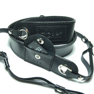 May include: Black leather camera strap with a small pocket for a memory card. The strap has a silver metal ring and the text "CZART" is embossed on the strap.