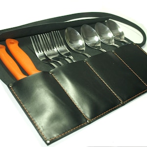 以下が含まれることがあります： オレンジ色の柄のナイフ、フォーク、スプーンが入った黒い革製のカトラリーロール。ロールはオレンジ色の糸でステッチされ、黒いストラップが付いています。カトラリーはステンレス鋼です。