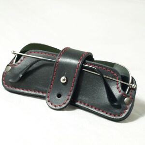 May include: A black leather sunglasses case with red stitching and a silver snap closure. The case is folded closed and the sunglasses are inside.