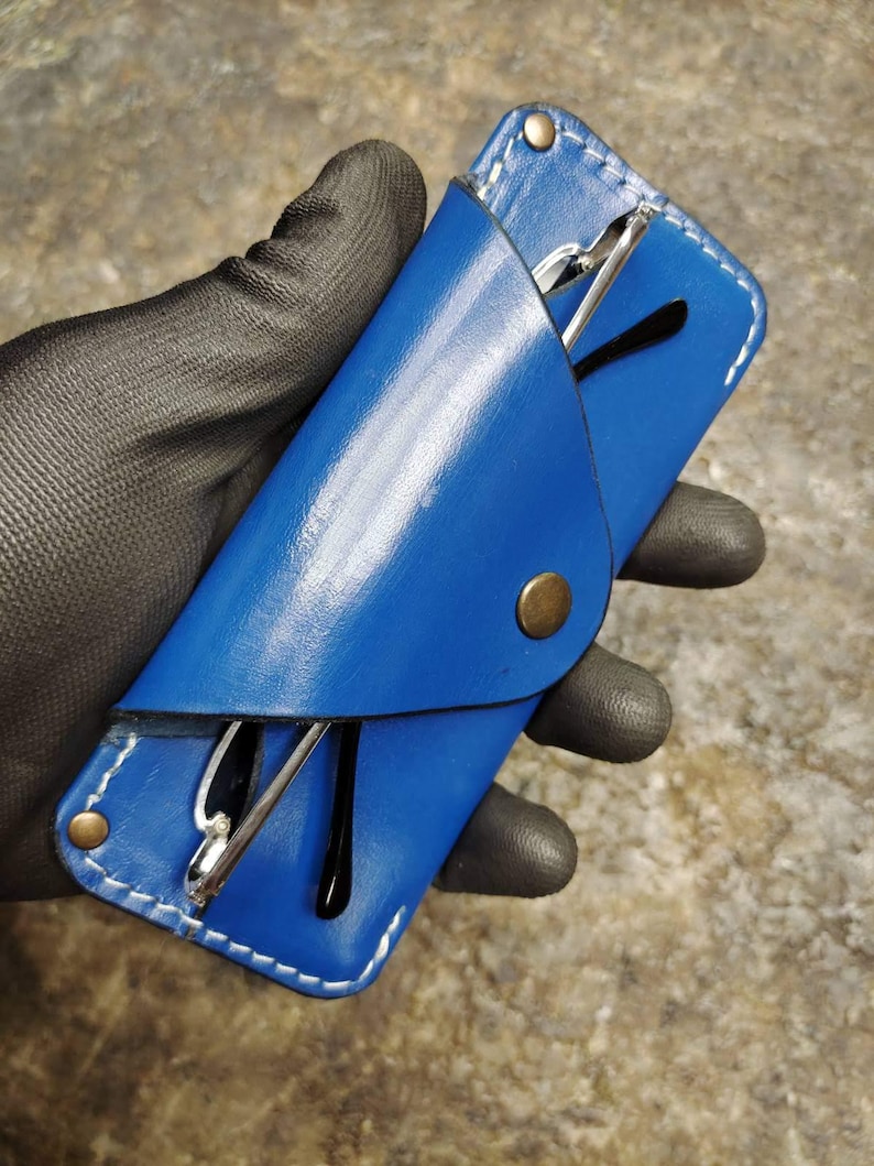 May include: A vibrant blue leather glasses case with white stitching and a brass snap closure. The case holds a pair of eyeglasses with black frames and silver arms. The case is designed to protect eyewear.