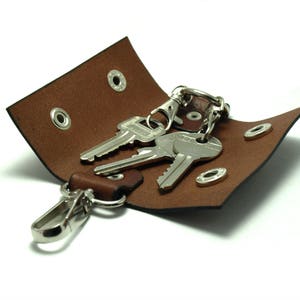 May include: A brown leather key holder with three keys attached to a silver key ring. The key holder has two metal eyelets and a snap closure.