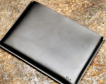 May include: Black leather laptop sleeve with a stitched edge and the initials "SLA" embossed on the front.