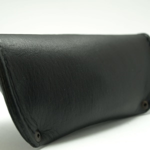 K&ouml;nnte beinhalten: Ein schwarzes Lederetui f&uuml;r Brillen oder Sonnenbrillen. Das Etui hat ein schlichtes Design und ist aus hochwertigem Leder gefertigt.