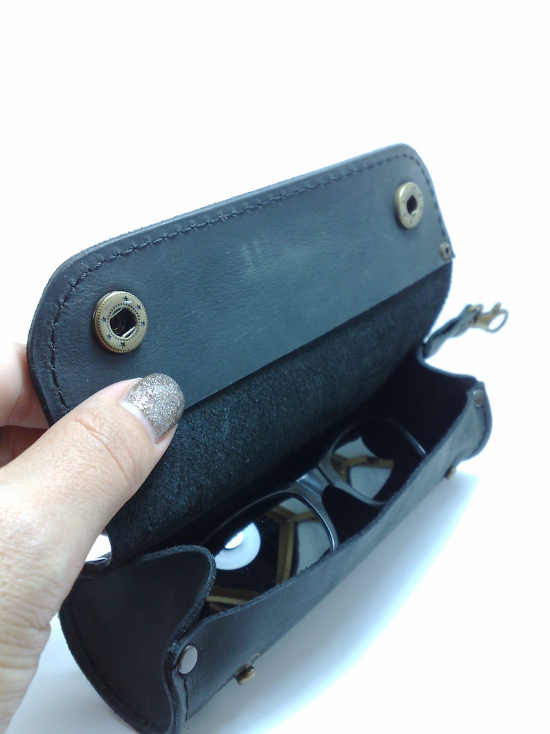May include: A black leather sunglasses case with a flap that opens to reveal a pair of sunglasses inside.