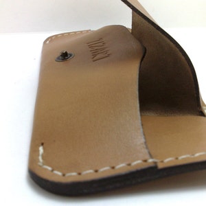 May include: A tan leather wallet with a snap closure and white stitching. The interior is a lighter shade of tan. The word "IZKI" is embossed on the inside. The wallet is open, revealing the interior.