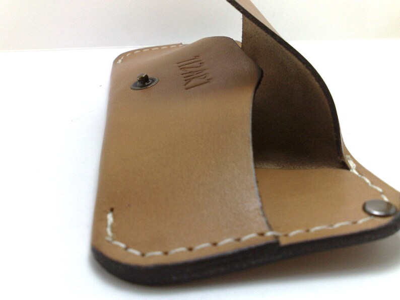 May include: A tan leather wallet with a snap closure and white stitching. The interior is a lighter shade of tan. The word "IZKI" is embossed on the inside. The wallet is open, revealing the interior.