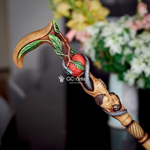 May include: A wooden walking stick with a carved snake wrapped around a red apple. The stick is decorated with green leaves and a carved human face.