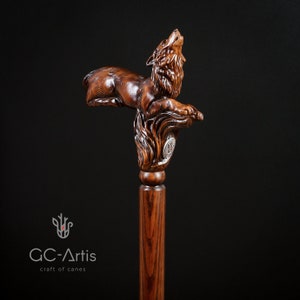 May include: A wooden walking stick with a detailed carving of a wolf howling at the moon. The wolf is carved in a realistic style and the stick is made of dark wood.