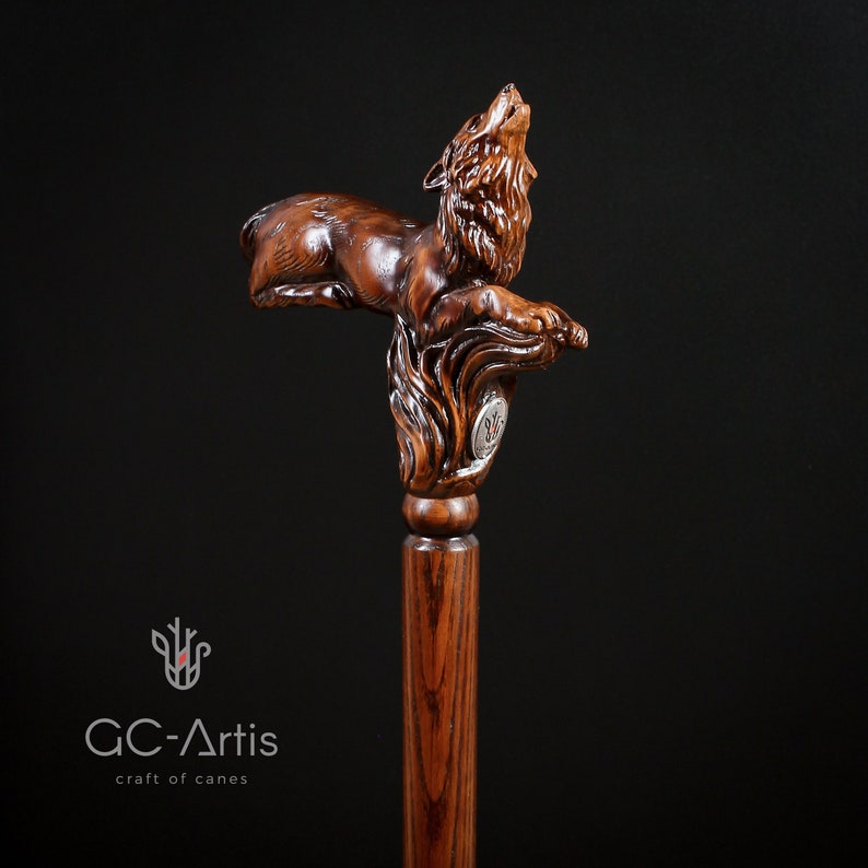 May include: A wooden walking stick with a detailed carving of a wolf howling at the moon. The wolf is carved in a realistic style and the stick is made of dark wood.