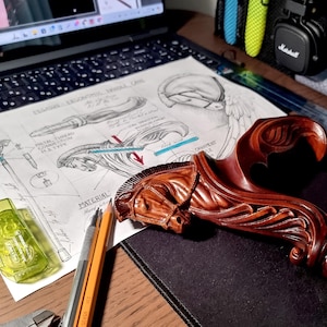 May include: A dark brown carved wooden handle shaped like a Pegasus head with a flowing mane, resting on a technical drawing titled Pegasus Ergonomic Handle Cane. The sketch includes labels like Metal Thread Connection M8 Type and Material Hard Wood.