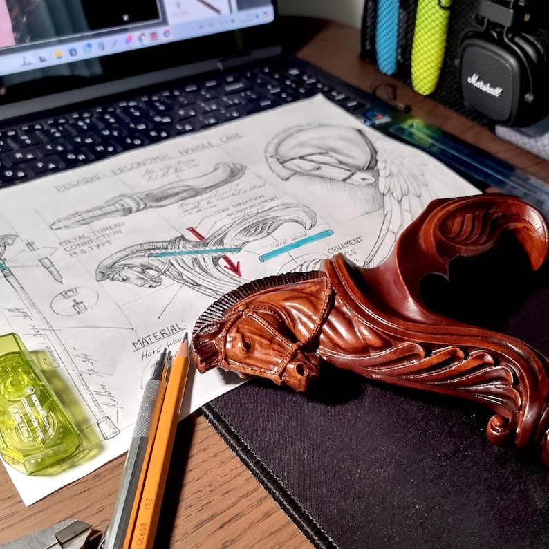 May include: A dark brown carved wooden handle shaped like a Pegasus head with a flowing mane, resting on a technical drawing titled Pegasus Ergonomic Handle Cane. The sketch includes labels like Metal Thread Connection M8 Type and Material Hard Wood.