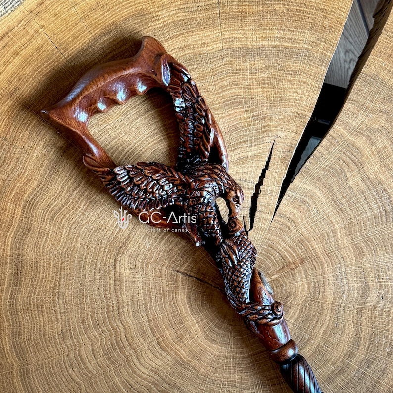 May include: A wooden walking stick with a carved eagle design. The eagle is in flight and has detailed feathers. The stick is brown and has a smooth finish.