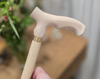 Könnte beinhalten: Hellfarbiger Holzspazierstock mit gebogenem Griff und Messingringdetail. Der Stock ist aus hellfarbigem Holz gefertigt und hat eine glatte Oberfläche. Der Griff ist ergonomisch für einen bequemen Griff gestaltet. Es ist eine Mobilitätshilfe.