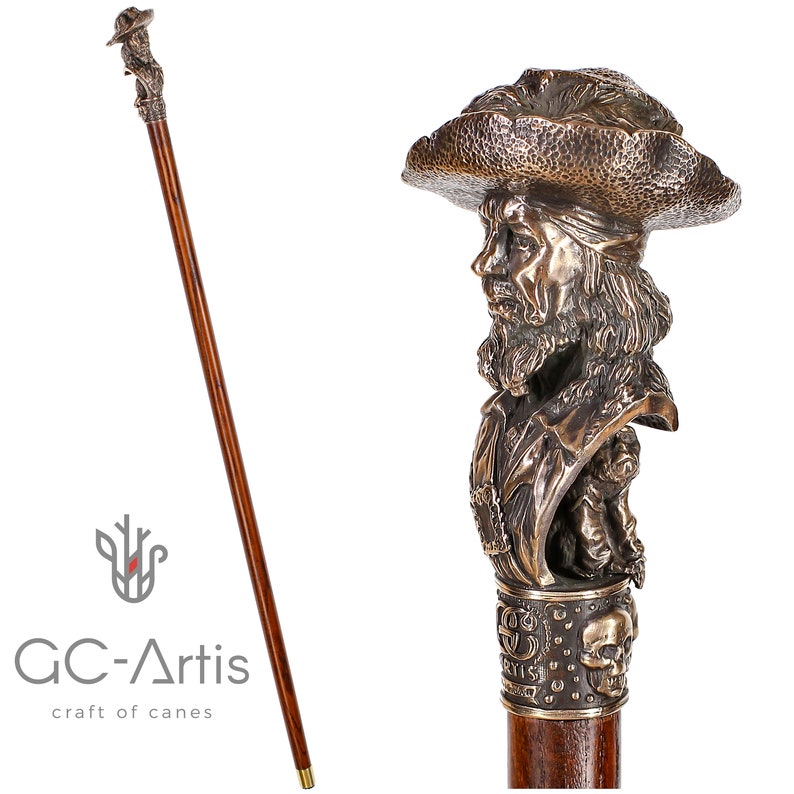 May include: A wooden walking stick with a bronze bust of a pirate wearing a hat and holding a sword. The bust is detailed with a beard, mustache, and a bandana. The stick has a skull and crossbones design at the bottom.