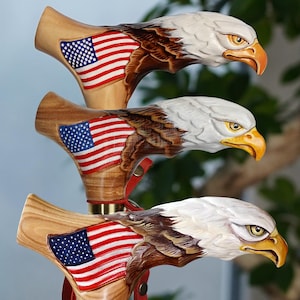 May include: Three wooden cane handles carved into the shape of bald eagle heads. Each handle features a hand-painted American flag on the side, with white, brown, and yellow details on the eagle head, and a brass-colored metal collar at the base.