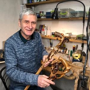 Photo 11
Portrait of artisan seated in workshop holding the finished snake-skull cane. Surrounded by woodworking tools, the craftsman highlights handmade authenticity and precision of GC-Artis canes.