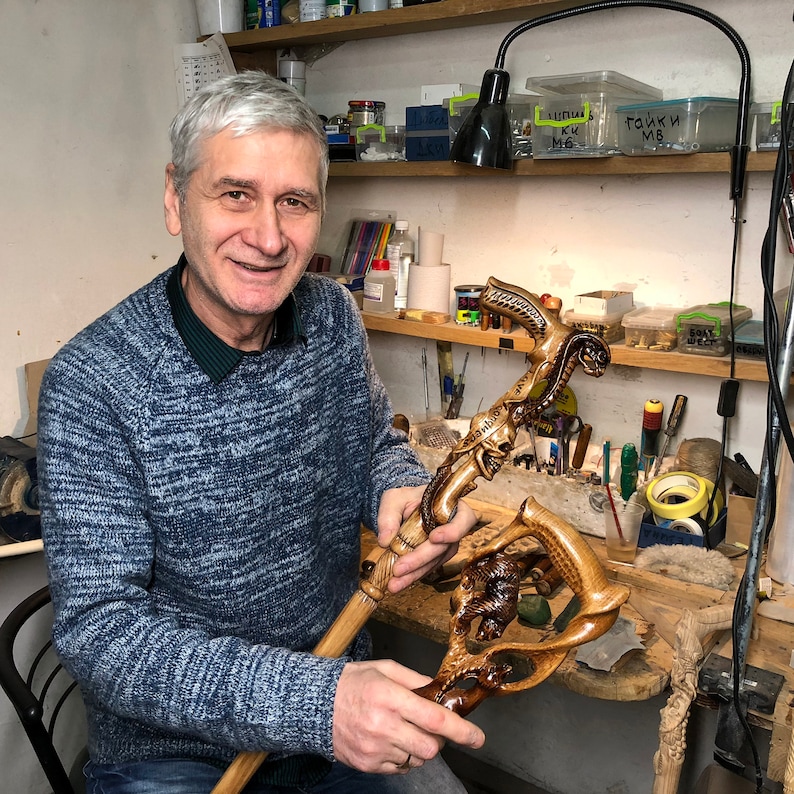 Photo 11
Portrait of artisan seated in workshop holding the finished snake-skull cane. Surrounded by woodworking tools, the craftsman highlights handmade authenticity and precision of GC-Artis canes.