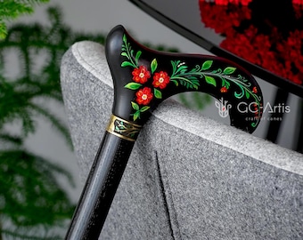 Puede incluir: Un bastón negro con un diseño floral pintado a mano. El mango es curvo y presenta flores rojas y hojas verdes. El texto "GC Artis craft canes" es visible en el bastón.