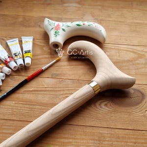Puede incluir: Un bast&oacute;n de madera con un acabado de madera natural y una banda de lat&oacute;n. El bast&oacute;n tiene un mango curvo y se est&aacute; pintando con pinturas acr&iacute;licas. El texto "GC-Artis craft of canes" es visible en el bast&oacute;n.