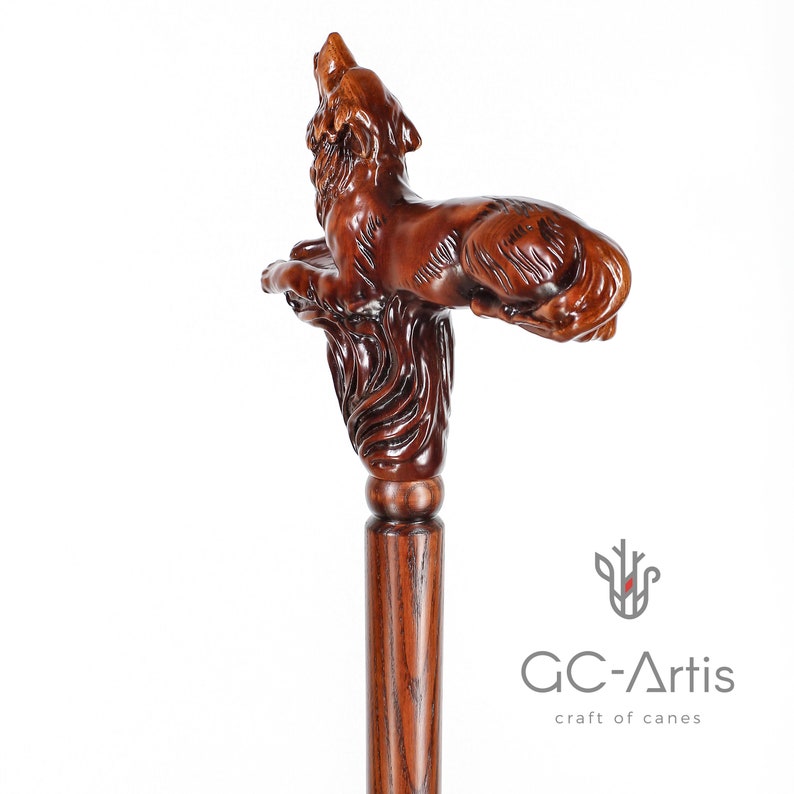 May include: A wooden walking stick with a detailed carving of a wolf howling at the moon. The stick is brown and has a smooth finish. The wolf is carved in a realistic style and has a detailed face and fur.