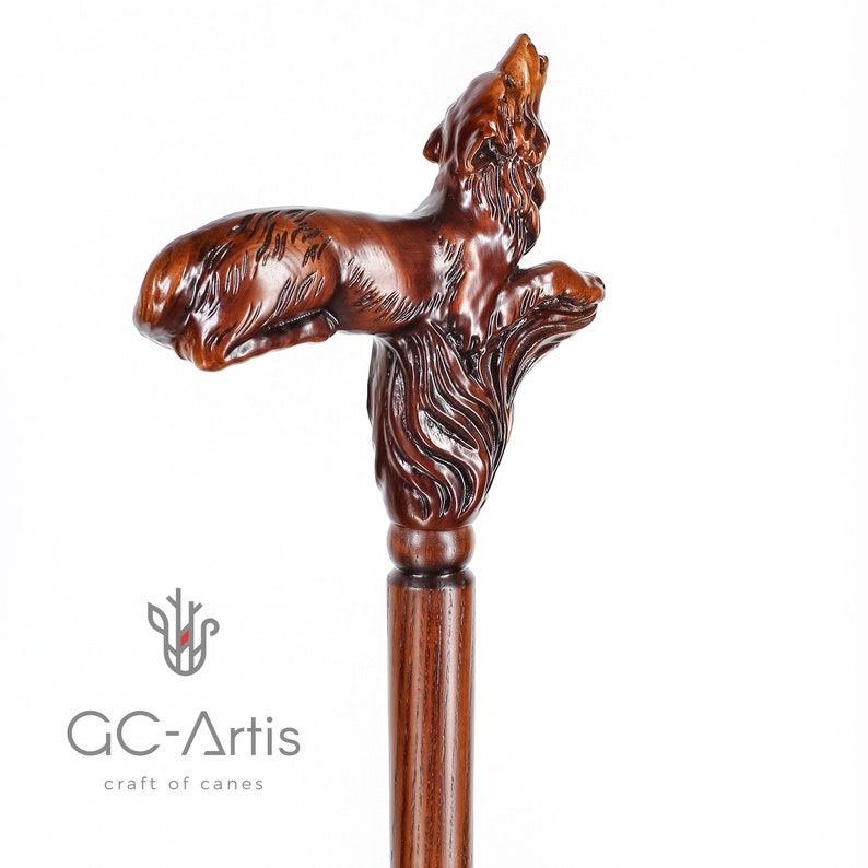 May include: A wooden walking stick with a detailed carving of a wolf howling at the moon. The stick is brown and has a smooth finish.
