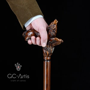 May include: A wooden walking stick with a carved wolf head handle. The wolf is howling and has a detailed, realistic design. The stick is brown and has a smooth finish.