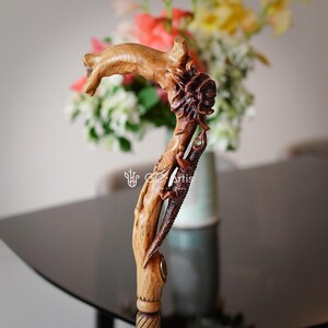 Indoor photo of the Floral Lizard cane placed on a table near a vase of flowers. The carved handle’s natural curves and painted floral accents match the soft indoor colors. The warm wood grain and detailed carving show the cane as a decorative piece as well as a functional support tool.