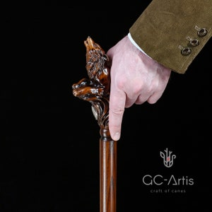 May include: A wooden walking stick with a detailed carving of a wolf howling at the moon. The stick is brown and has a smooth finish.