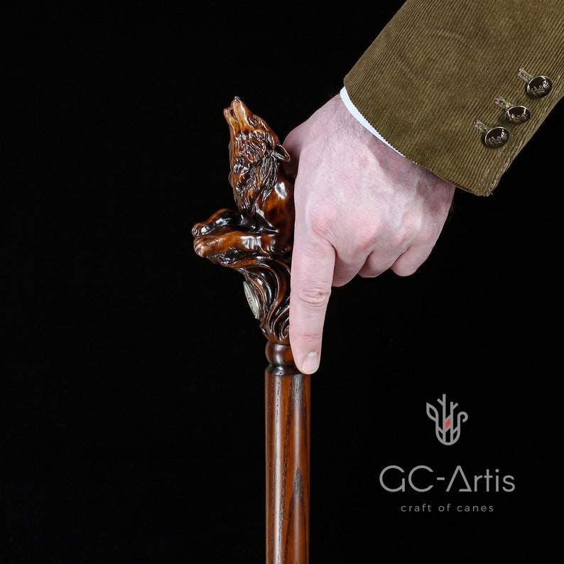 May include: A wooden walking stick with a detailed carving of a wolf howling at the moon. The stick is brown and has a smooth finish.