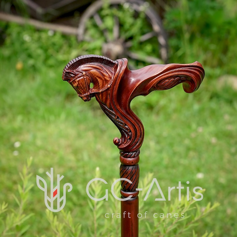 May include: A dark brown wooden walking cane featuring a detailed hand-carved horse head handle. The handle displays a sculpted equine profile with a mane and bridle, transitioning into a smooth, straight shaft with a decorative twisted collar.