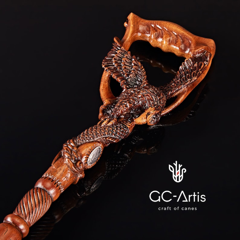 May include: A wooden walking stick with a detailed carving of an eagle. The handle is shaped like an eagle's head and wings, and the shaft is intricately carved with feathers. The stick is a dark brown color and has a polished finish.